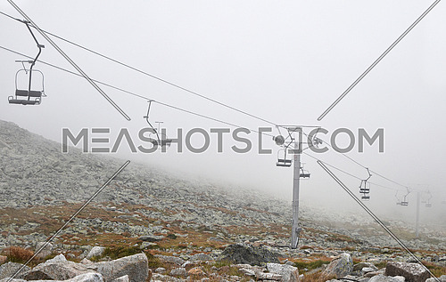 Mountain cableway chairlift in clouds and fog, high angle side view