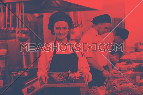 female Chef  in hotel or restaurant kitchen holding grilled beef steak plate with vegetable decoration