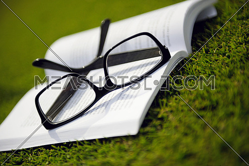 Glasses on a book outside with grass inbbacground, education relax and study concept