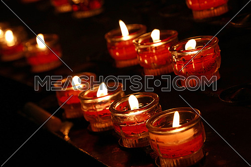 Red translucent glass candles burning in dark church, close up, high angle view