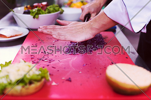 master chef hands cutting salad for a burger in the rastaurant kitchen
