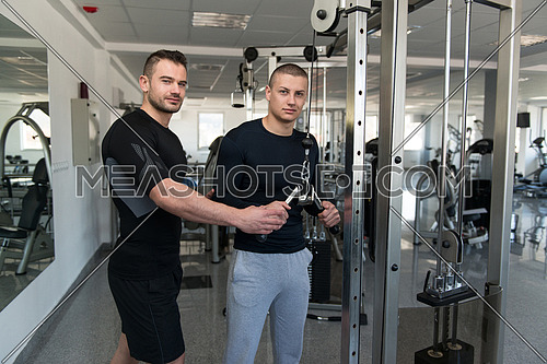 Personal Trainer Showing Young Man How To Train Triceps On Machine In The Gym