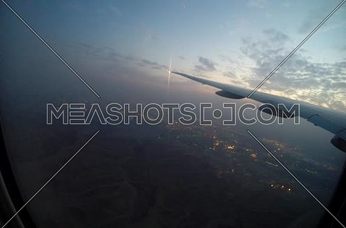 shot from plane window showing wing while flying over a city   at sunset