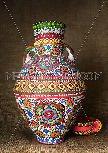 A colorful Egyptian handcrafted artistic ornate pottery jar on a sackcloth background. one of the art works of Ebtessam ElGohary, a contemporary Egyptian artist specialized in pottery painting art. Decorations are inspired by the Mandala style