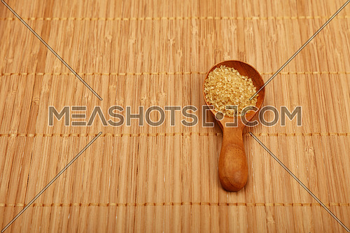 Wooden round scoop spoon of brown cane sugar on bamboo mat background
