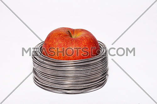 Wired apple: whole red apple in coils of aluminum wire isolated on white background