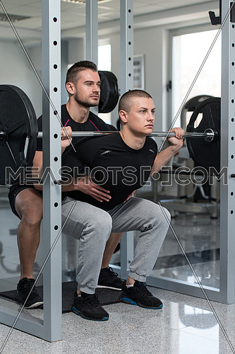 Personal Trainer Showing Young Man How To Train Barbell Squats Exercise In A Health And Fitness Concept