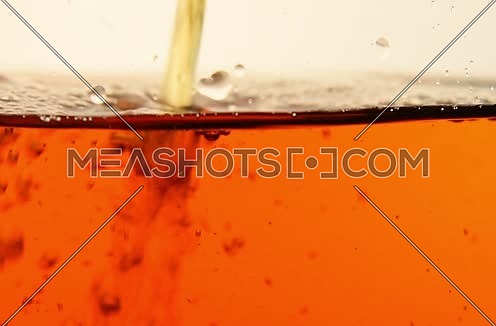 Stream of red black tea poured in transparent glass teapot, air bubbles flow when filling, slow motion, extreme close up, low angle side view