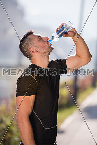 Athlete man drinking water from a bottle after jogging in the city on a sunny day