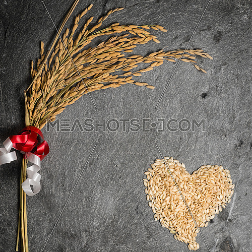 In the picture an ear of wheat and a heart formed by grains of rice on background of  stone.