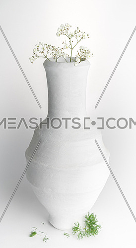 Still life composition of white pottery vase and small white flowers on white background