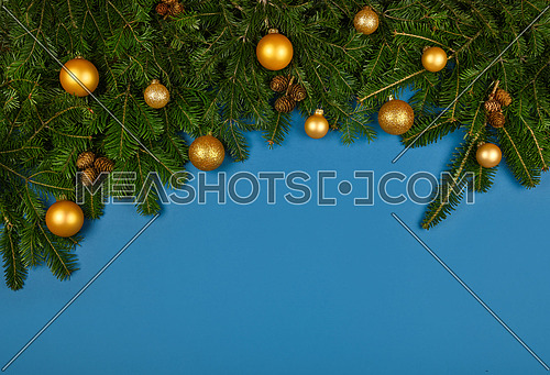 Close up fresh green spruce or pine Christmas tree branches decorated with cones, golden balls and baubles, over blue background with copy space