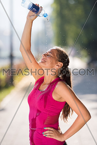 Athlete woman runner pouring water from bottle on her head after jogging in the city on a sunny day