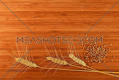 Wooden bamboo cutting board with three wheat ears and handful of ripe grains, add your text