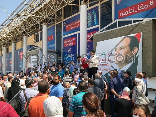 Cairo, Egypt - August 14 2021: Egyptian citizens at Exhibition land waiting for their turn to receive the Covid-19 coronavirus vaccine, with two of the organizers and background of Egyptian president