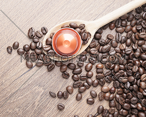 Coffee capsule on wooden spoon and roasted coffee beans on wooden background,top view,close up.