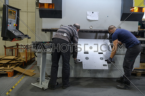 a two man working in a modern industry prepares material for processing on a CNC machine, wears a protective mask on his face due to a coronary virus pandemic. High quality photo