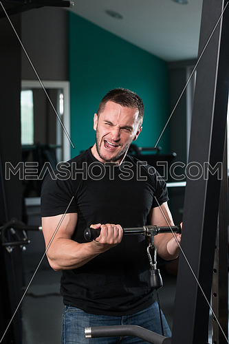Young Regular Man Wearing Jeans And T-Shirt Doing Heavy Weight Exercise For Biceps On Machine With Cable  In The Gym
