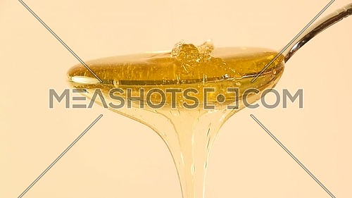Close up fresh thick fluid acacia honey pouring and flowing from metal spoon over beige background with copy space, low angle side view, slow motion