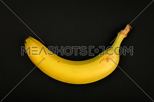One fresh ripe yellow banana isolated on black paper background, close up, elevated top view, directly above
