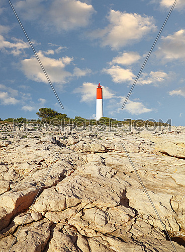 Rocky sea coast landscape with lighthouse over clear blue day sky, low angle view