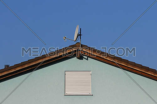 Blue on blue facade with simple window, ceramic tile roof line and satellite dish