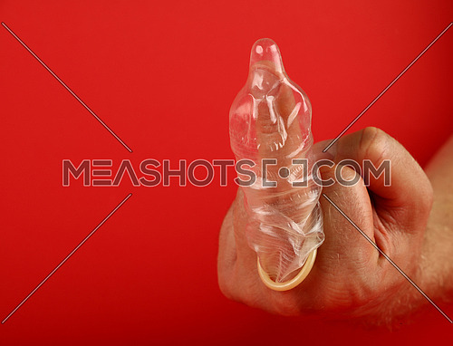 Close up man hand showing protest or insult rude gesture with latex condom on finger over red background with copy space, low angle side view