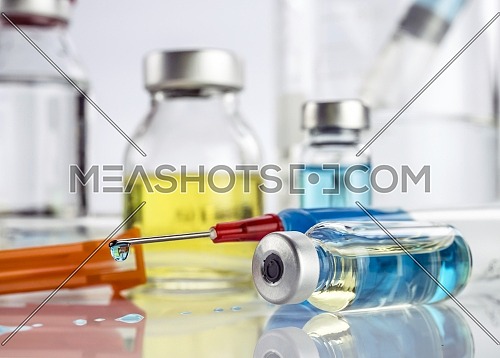 Syringe with medication drips next to vials in a hospital, conceptual image