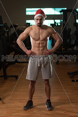 Portrait Of A Young Santa Claus Posing And Showing Bodybuilding Pose In Gym