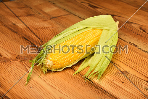 One open fresh yellow corn cob with green husk on brown vintage wooden surface