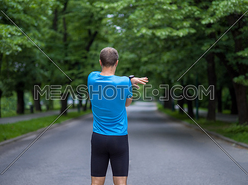 healthy male runner warming up and stretching in city park before morning training