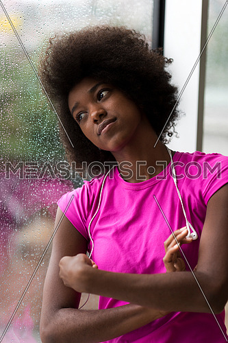 portrait of young afro american woman in gym on workout break while listening music on earphone  and dancing  rainy day and bad weather outdooor