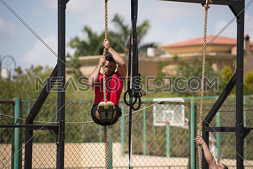 young middle eastern athletic man strenuous exercise climbing the rope outside on a sunny day