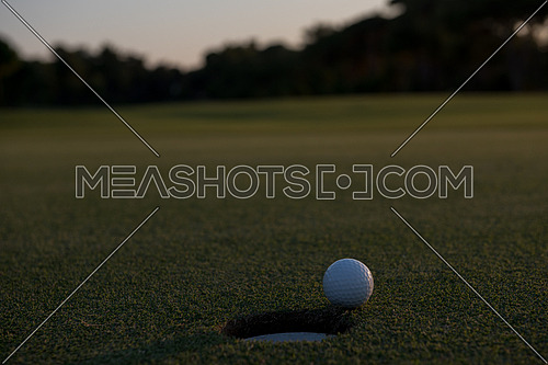 golf ball on edge of course hole representing achivement and success business concept, beautiful sunset in background