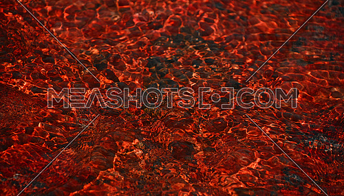 Abstract red color running water stream deflection flowing over stones texture background