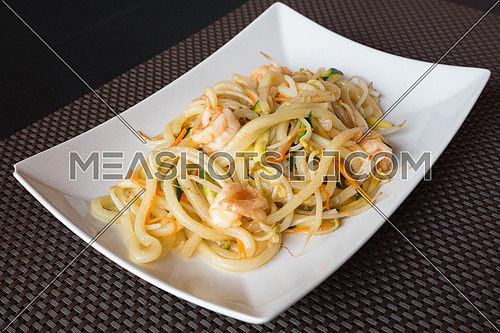 delicious japanese food yaki udon, noodles with seafood,shrips and vegetables,white plate on dark backgroung.