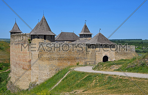 Medieval old fortress castle with ancient stone walls, wooden roofs and road, green hills and clear blue sky, Khotyn, Ukraine