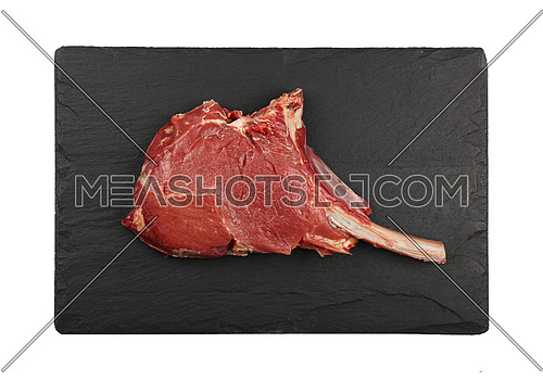 Close up one raw tomahawk ribeye beef steak with rib bone on black slate board isolated on white background, elevated top view, directly above