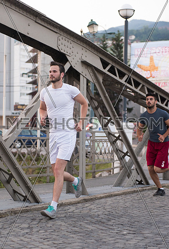 group of young sporty people jogging across the bridge at sunny morning in the city