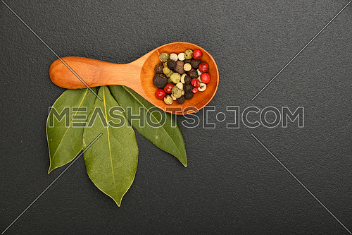 Group of three bay laurel leaves and mix of peppercorn in wooden scoop on black chalkboard background