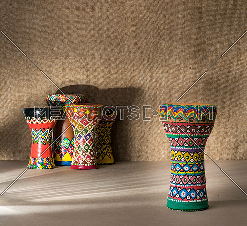 Decorated colorful pottery goblet drum on background of goblet drums, wooden table with vanishing shadow lines, and sackcloth wall. Low light shot