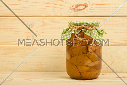 One glass jar of homemade pear compote with green checkered textile top decoration at beige painted vintage wooden surface
