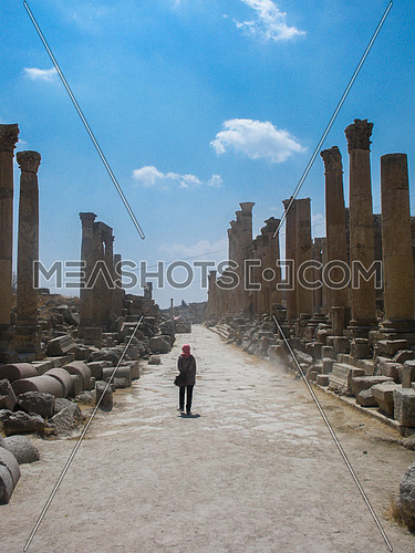 An arabian girl walking on the main path of the roman remains of Jarash surrounded with huge and a lot of stone poles in Jarash, Jordan