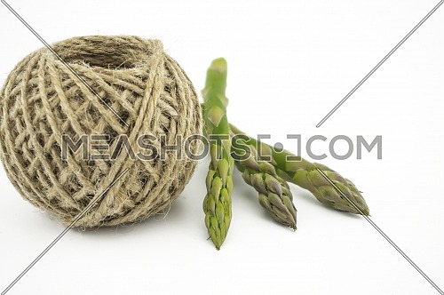 Fresh green asparagus spears near ball of natural hemp twine isolated on white background, selective focus in a low angle view