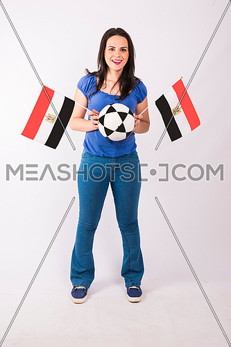 Young lady standing and holding two small egyptian flags, and ball on white background.