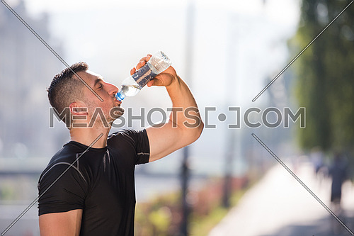 Athlete man drinking water from a bottle after jogging in the city on a sunny day