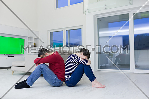 Cheerful young couple sitting with back to each other on floor at home