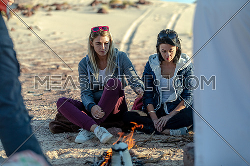 Female tourists sitting around bedouin bonfire exploring Sinai Trail in Ain Hodouda by day.