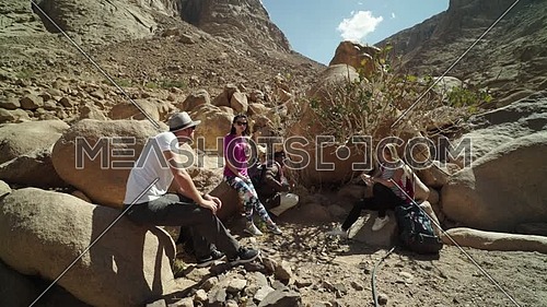 Follow shot for group of tourists get rest in the shade besides Almond tree with bedouin guide to explore Sinai Mountain for wadi Freij at day.
