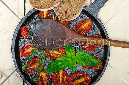 oven baked cherry tomatoes with basil and thyme on a cast iron skillet and wood spoon